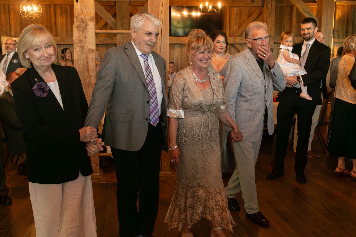 Elegantly dressed guests dancing and socializing at a rustic barn wedding reception venue.
