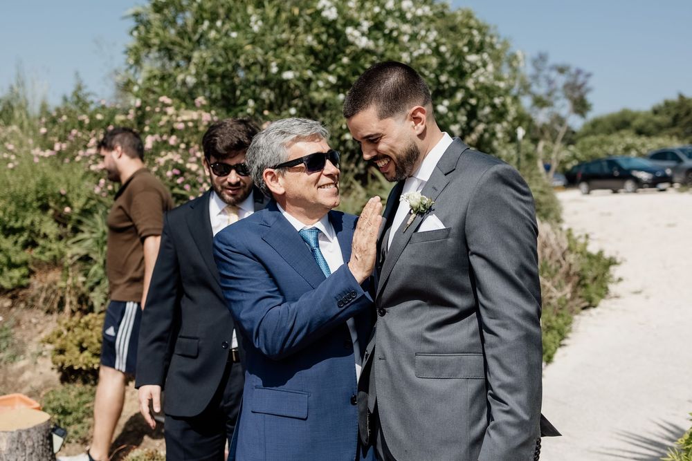 Two people in formal suits share an emotional moment together outdoors on a sunny day.