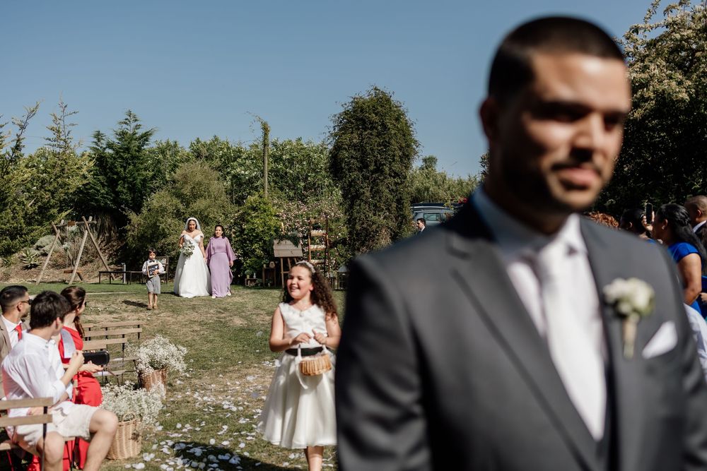 Wedding guests celebrate outdoors in a sunny garden setting with natural greenery and trees in the background.