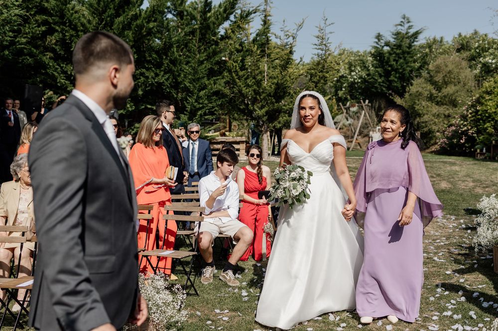 Wedding party members walk and celebrate together outdoors on a sunny day at a rustic venue.
