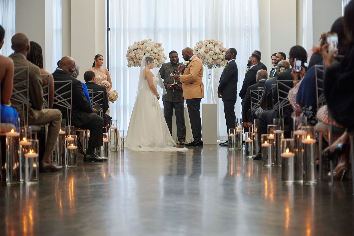 Wedding guests line both sides of an aisle during a ceremony in an elegant indoor venue with modern decor.