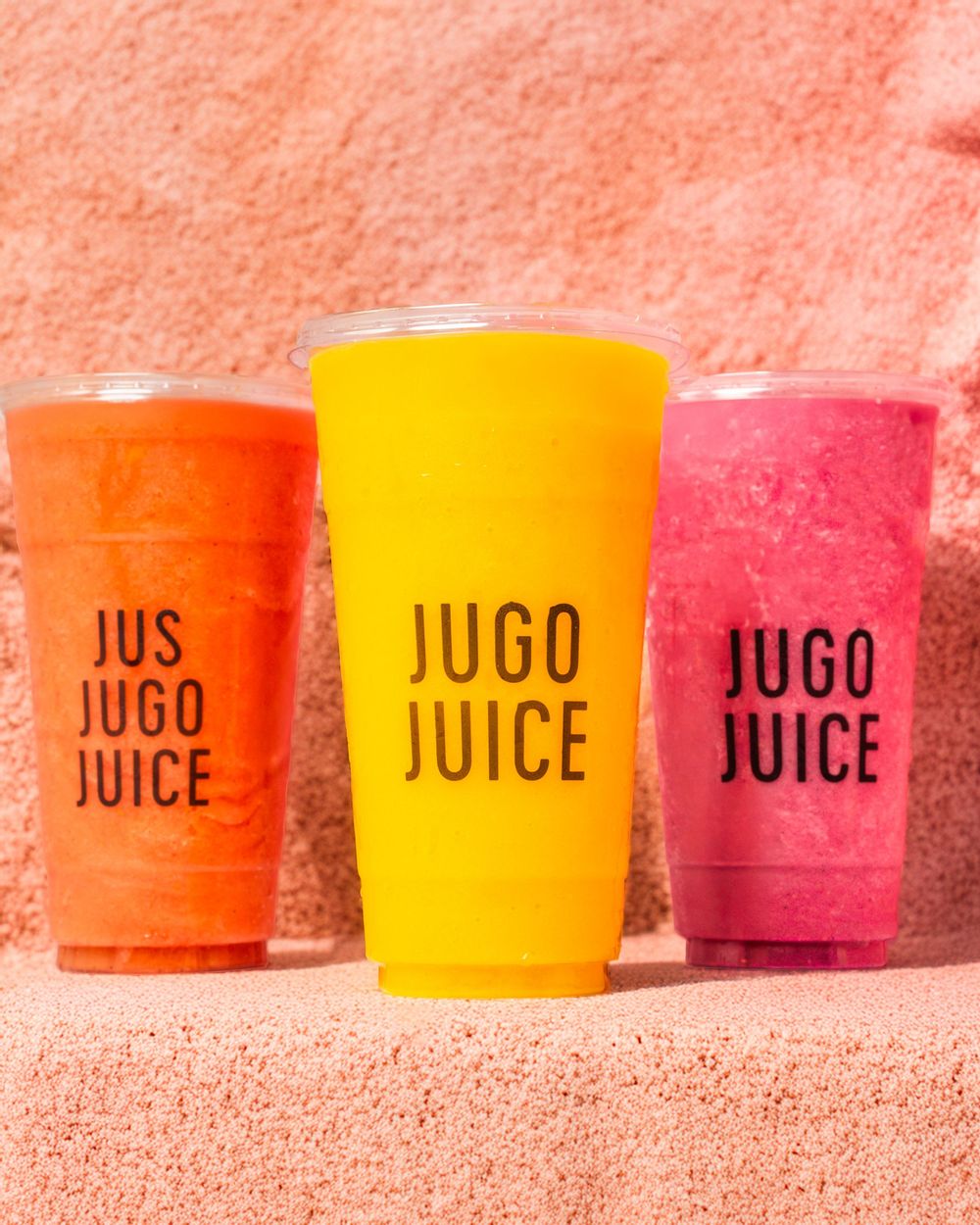 Colorful juice cups in orange, yellow and pink arranged in a row against a coral-colored background.