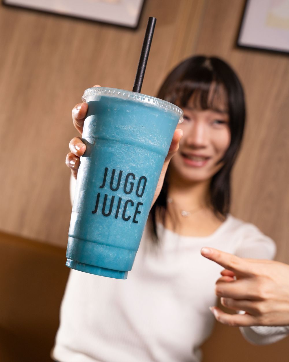 Someone holds up and points to a bright blue frozen drink in a clear plastic cup with "JUGO JUICE" branding.