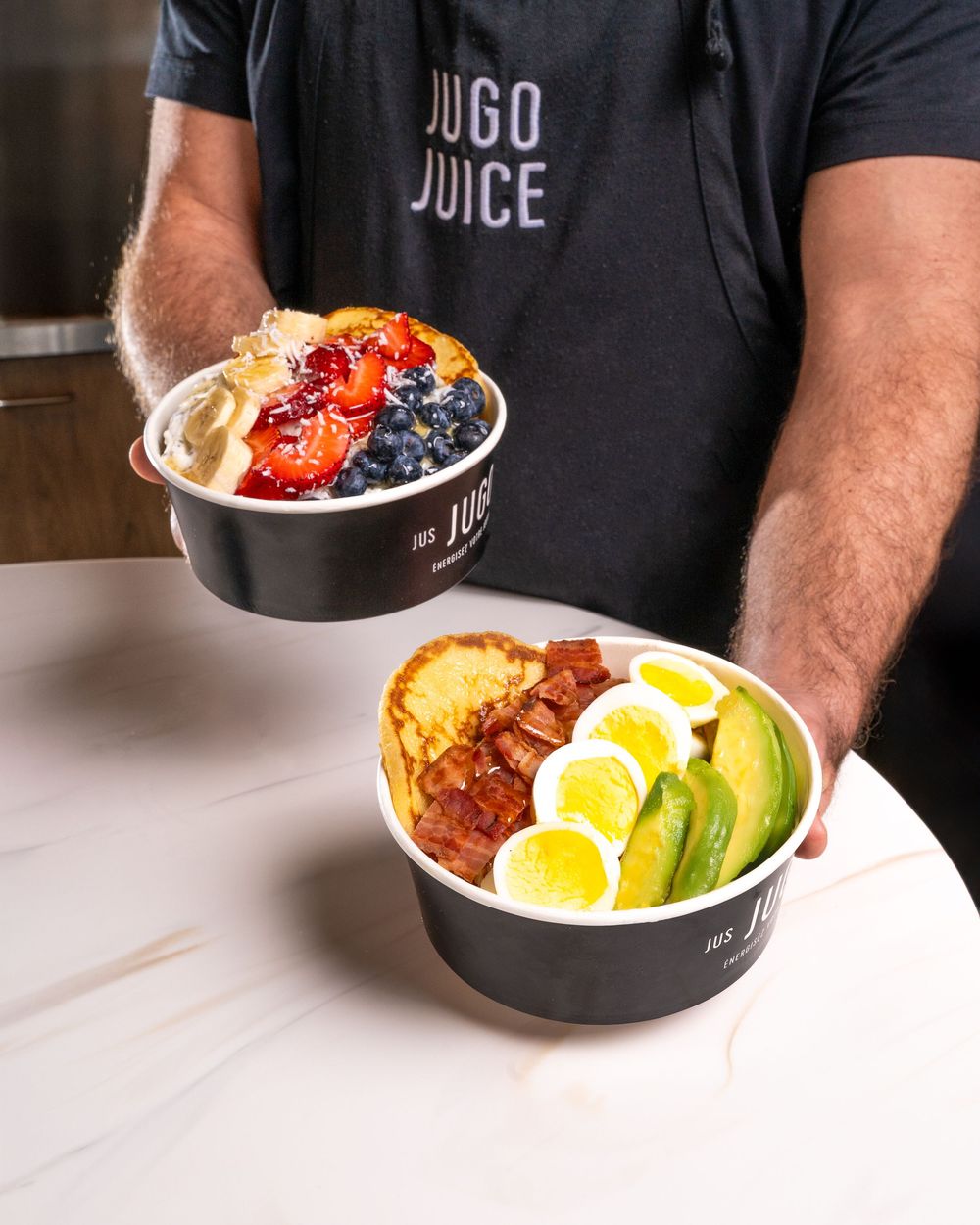 Bowl of yogurt topped with fresh berries, granola, hard boiled eggs, and avocado slices on white surface.