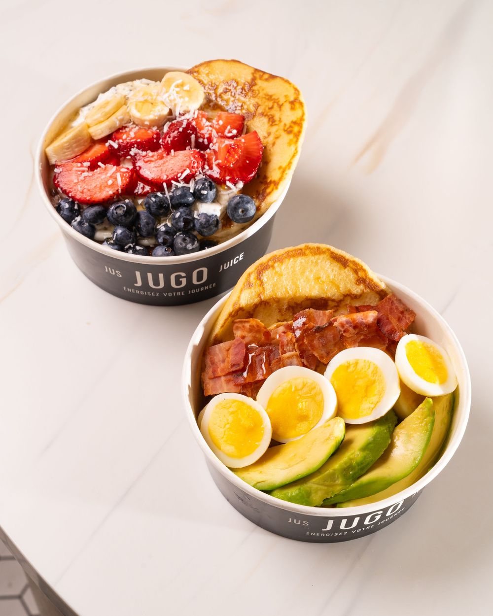 Fresh acai bowl topped with colorful fruits, berries, and granola served in a dark bowl on marble surface.