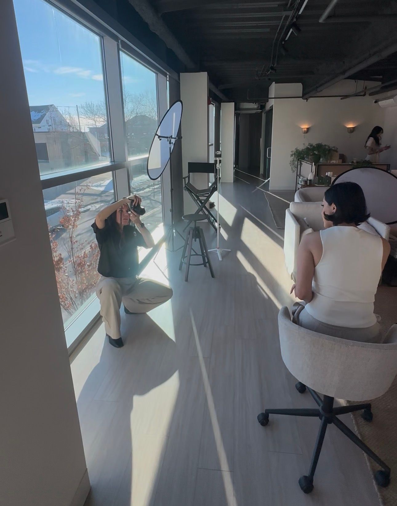 A photo shoot setup in a bright office space with reflectors and natural light streaming through large windows.