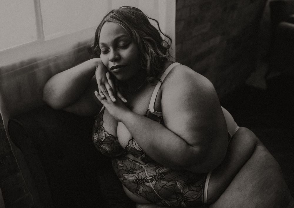Black and white boudoir portrait of a plus-size woman in lingerie posing gracefully on a couch.