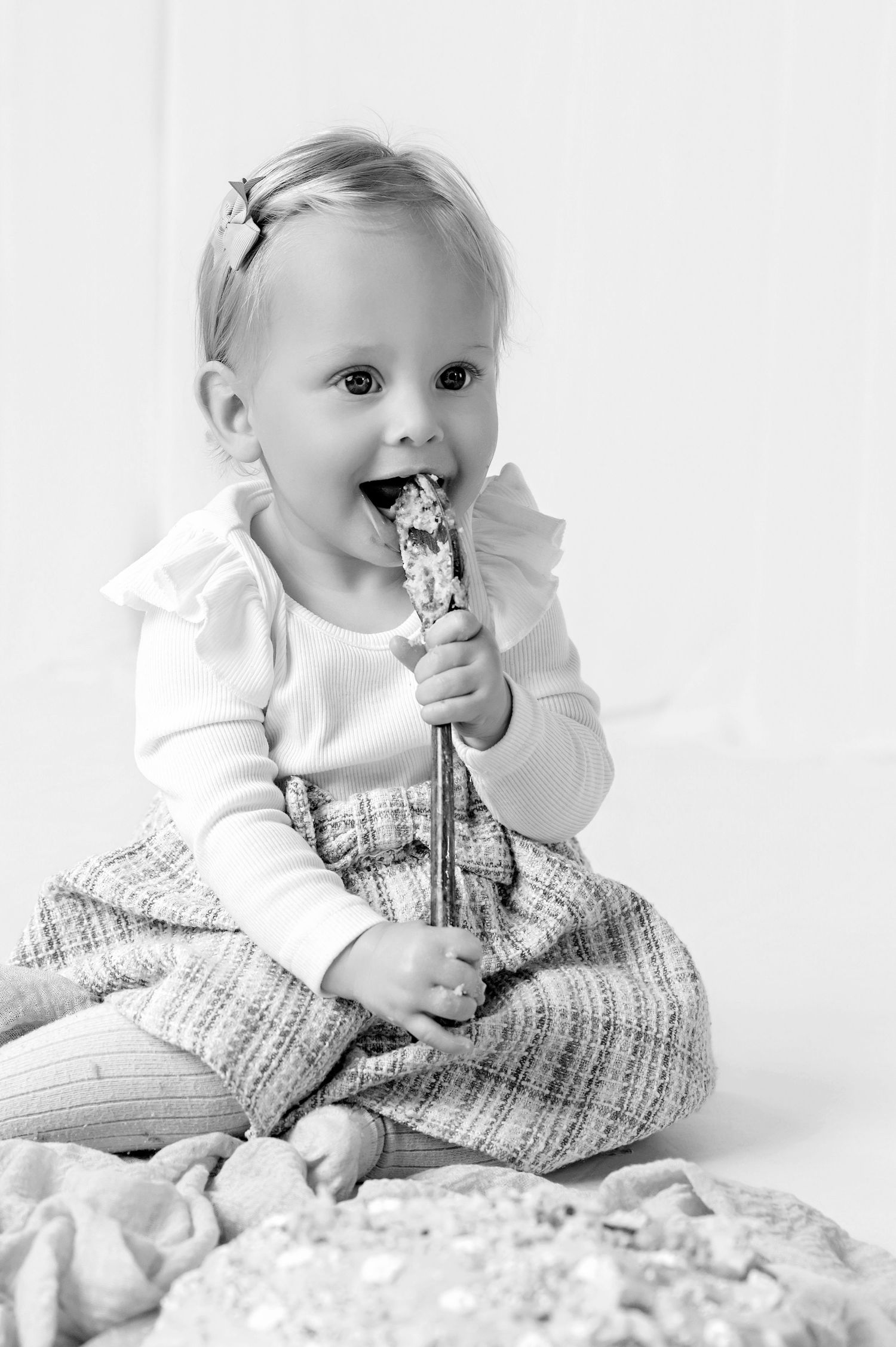 Adorable blonde toddler girl in pink skirt eating a decorated cake pop at a birthday celebration.