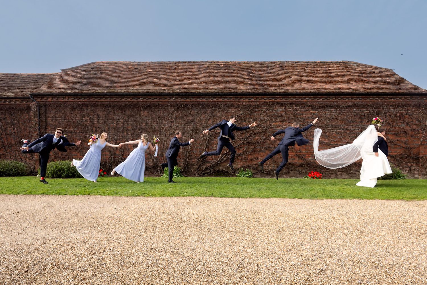 Wedding party members playfully pose with flowing white fabric against a rustic farm backdrop during a photo session.