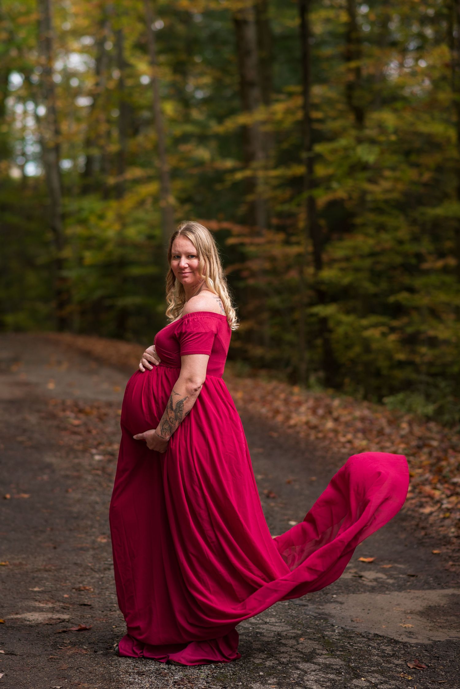 A woman in a flowing red dress twirls gracefully in an autumn forest setting.