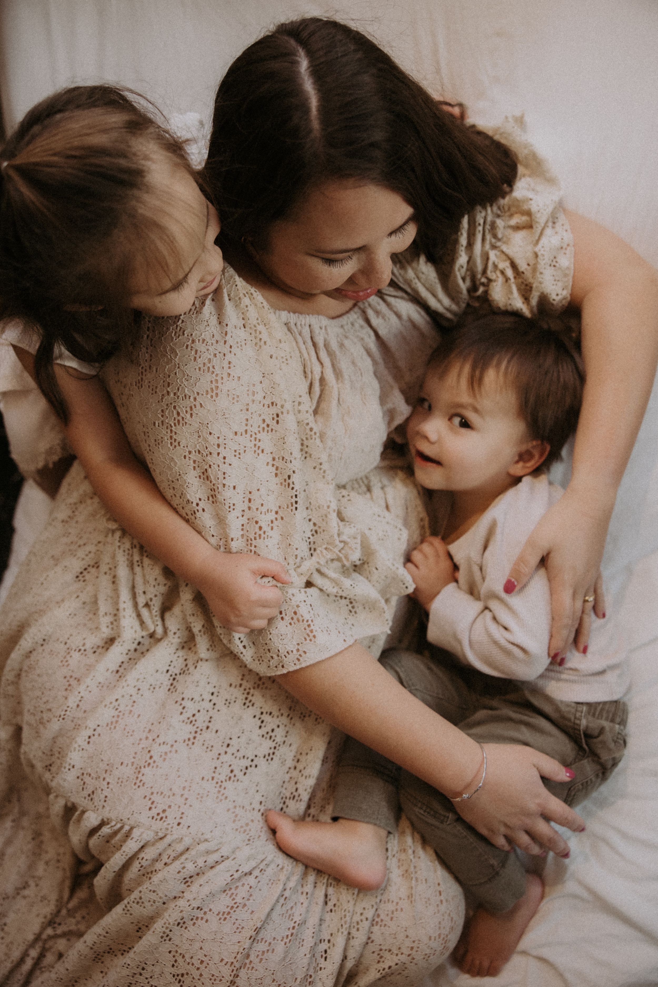 A tender family moment captured in warm tones as they cuddle together on a lace-covered bed.