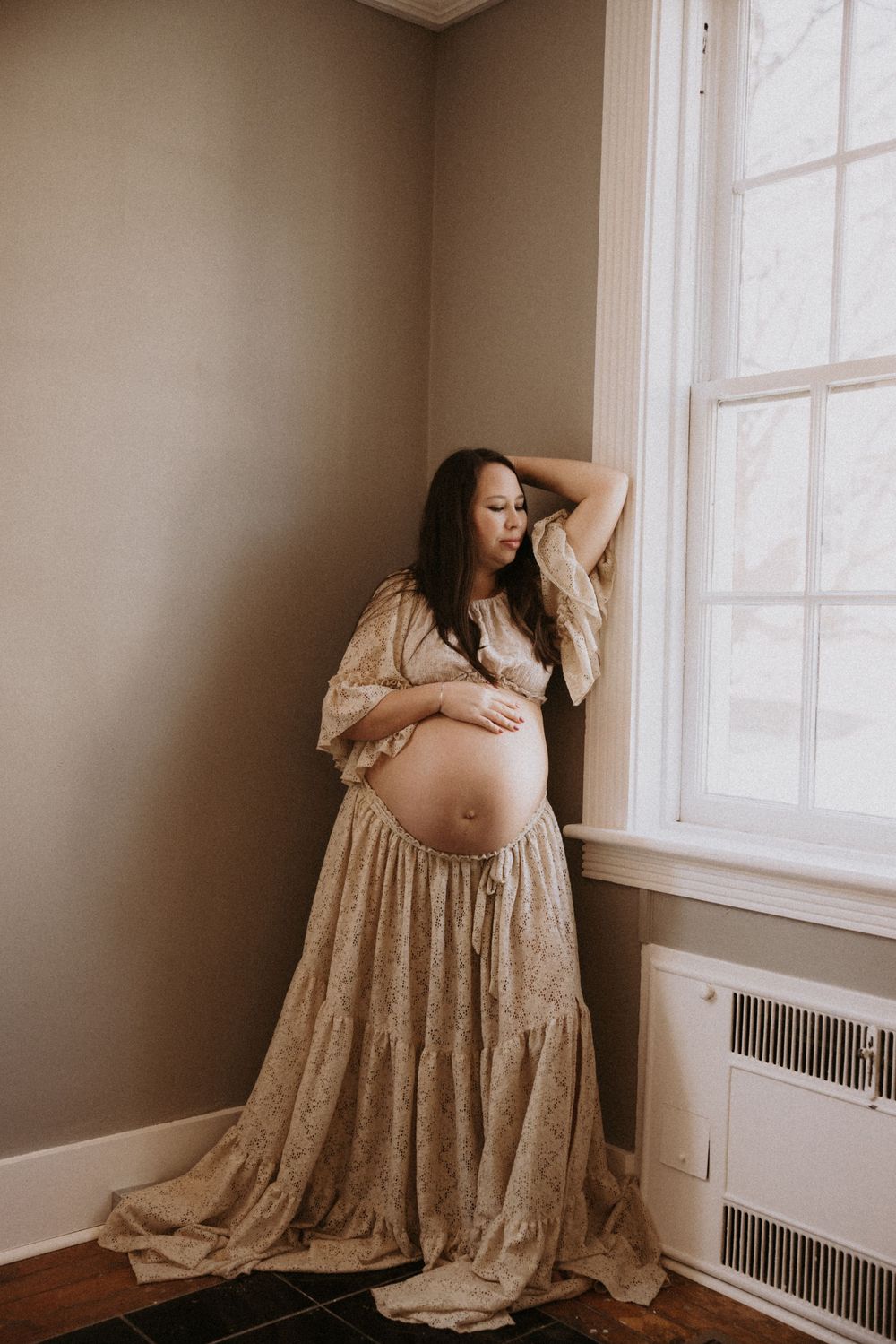 Maternity photoshoot in a beige lace dress by a window showing different angles of an expectant mother.
