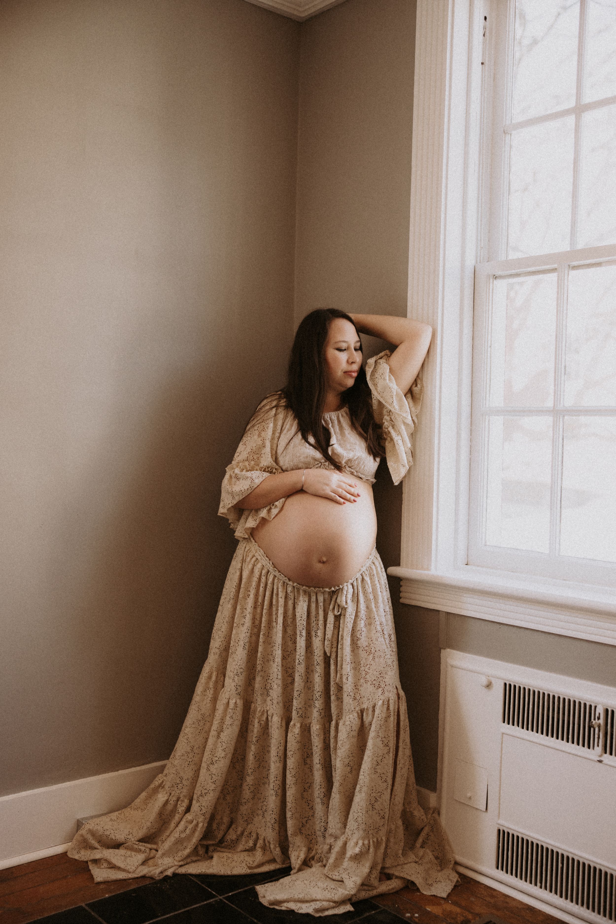 Maternity photoshoot in a beige lace dress by a window showing different angles of an expectant mother.