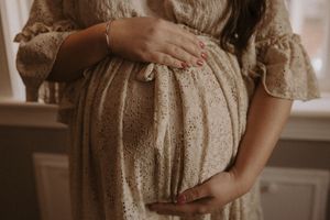 A person wearing a vintage-style beige lace dress stands in a sunlit room with soft, romantic lighting.