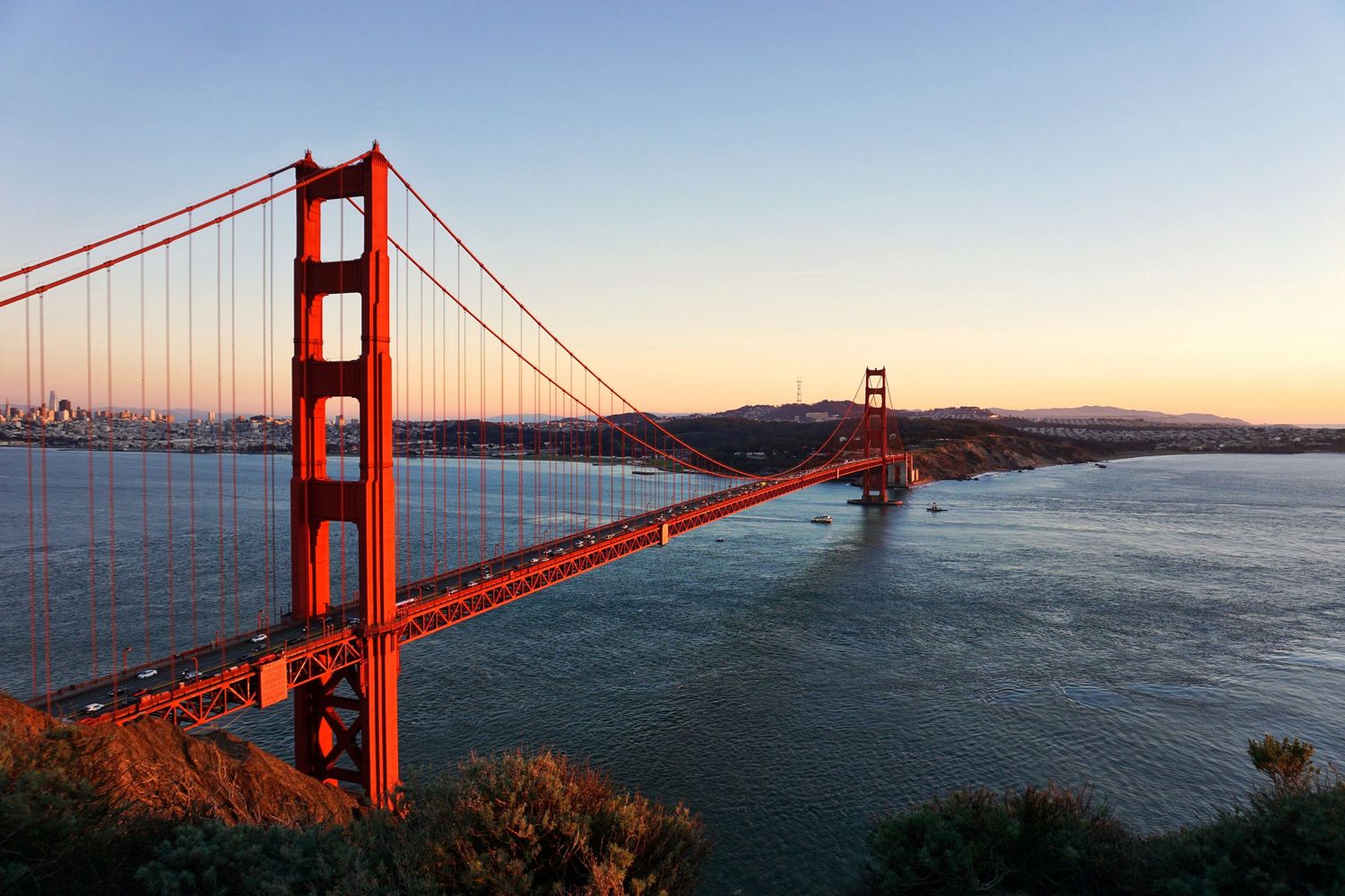 Golden Gate Bridge at sunset over San Francisco Bay, showcasing its iconic red towers and suspension cables.