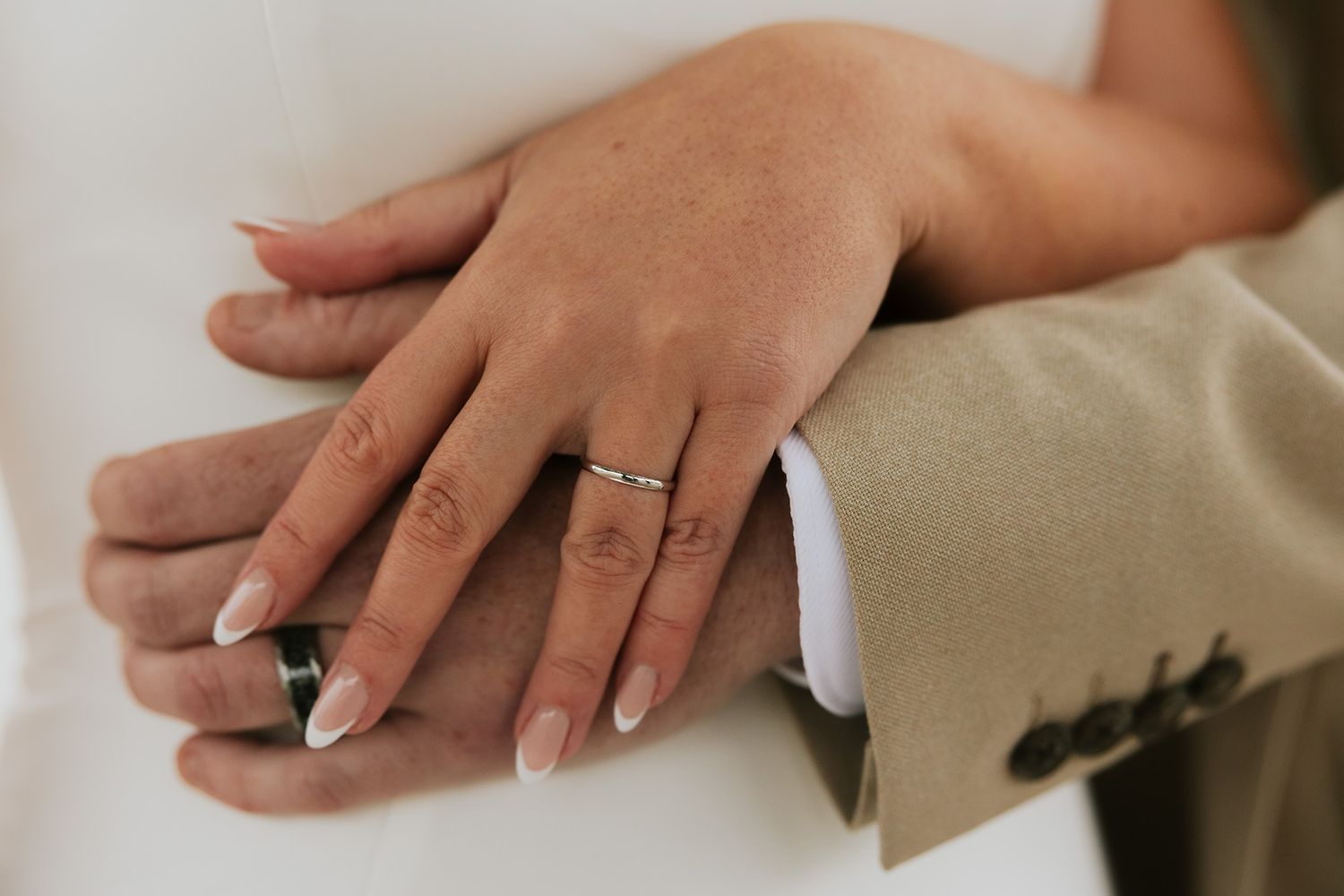 Close-up of bride and groom hands showing wedding rings, bride with French manicure nails.