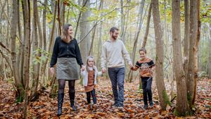 famille marchant en forêt en automne sur un chemin couvert de feuilles dans les Yvelines lors d’une séance photo