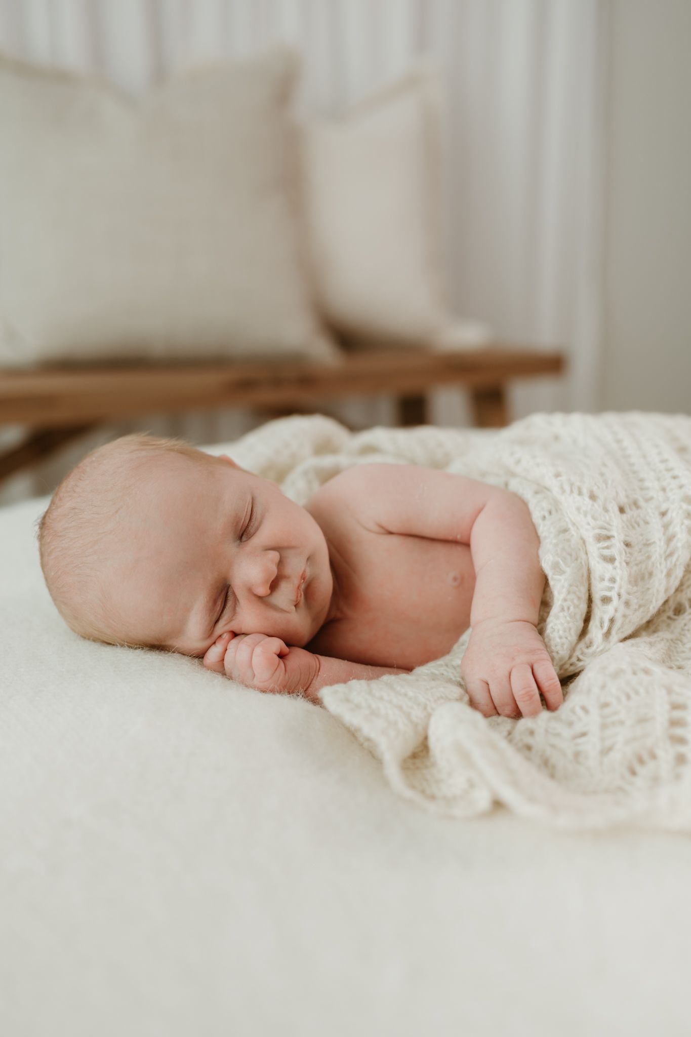 Peaceful newborn baby sleeping on a soft cream knit blanket in a bright, minimalist nursery setting.