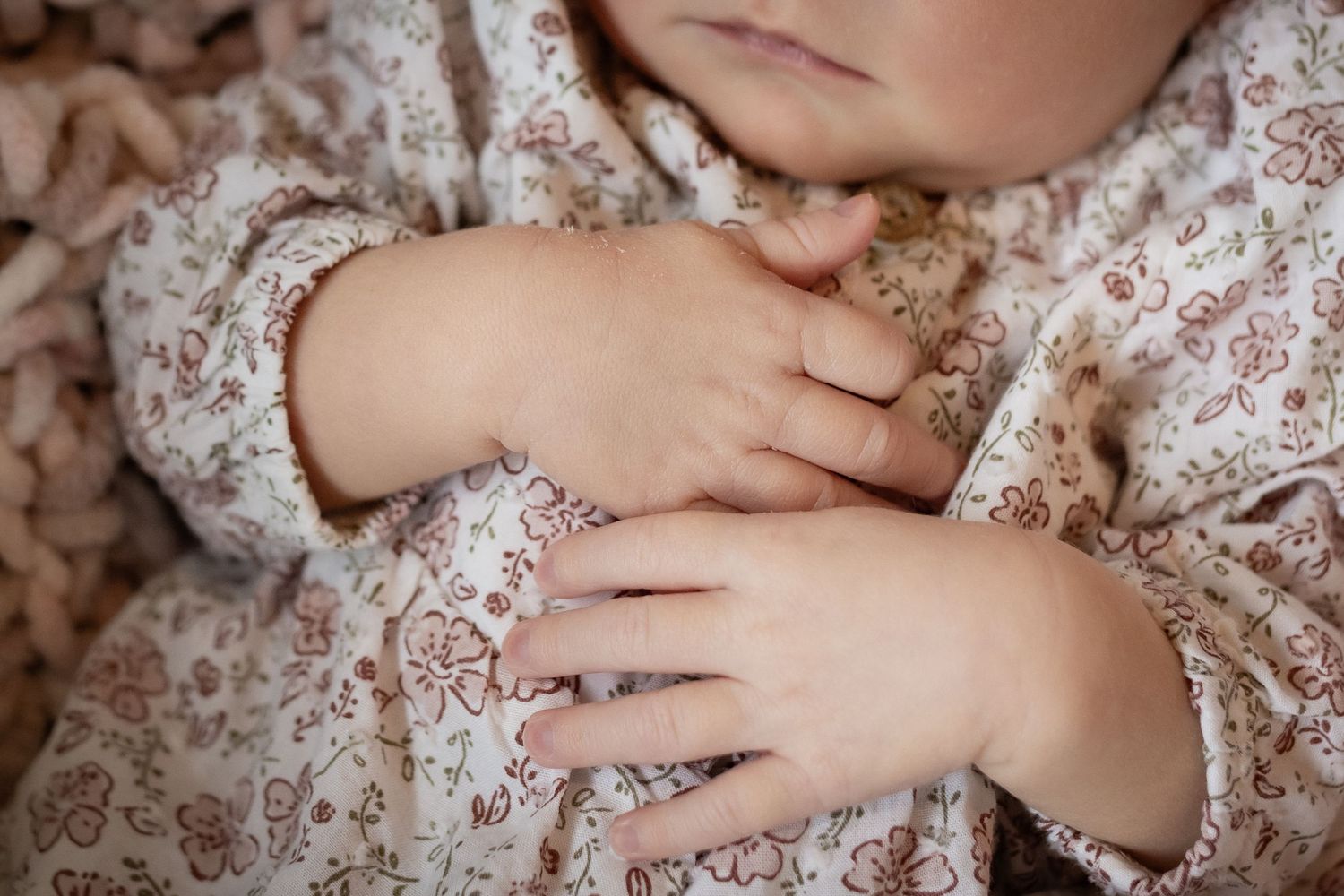 Close-up of sleeping newborn baby hands crossed over chest in floral outfit.