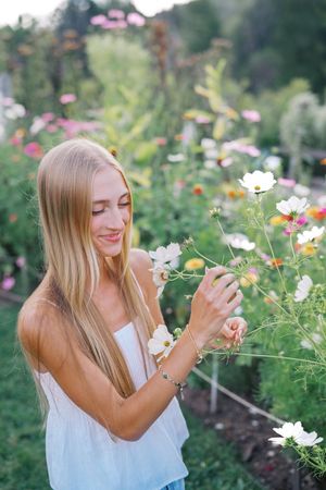 A person in white leans in to smell blooming flowers in a colorful garden.