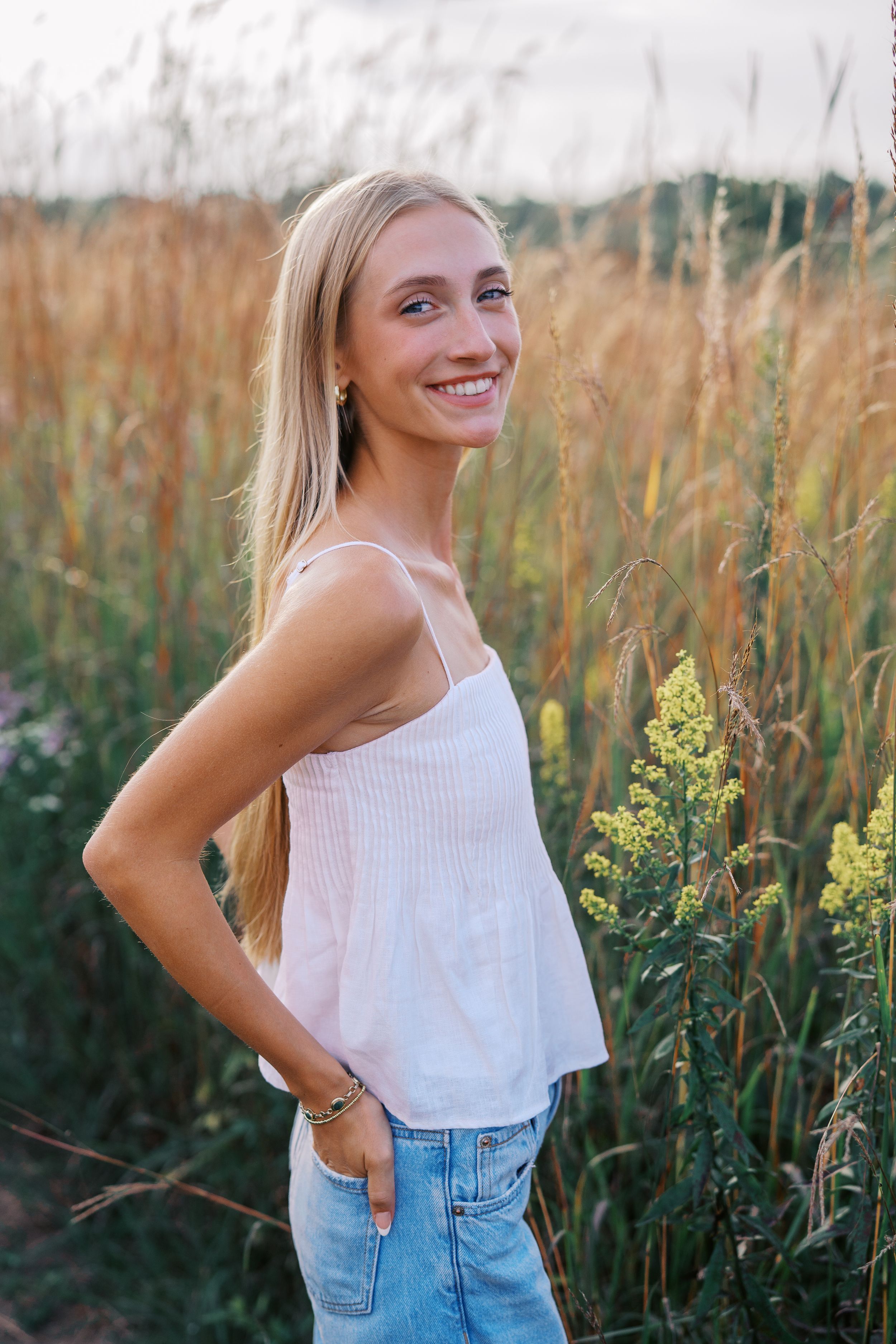 Summer portrait session in tall grass wearing a white tank top and denim.