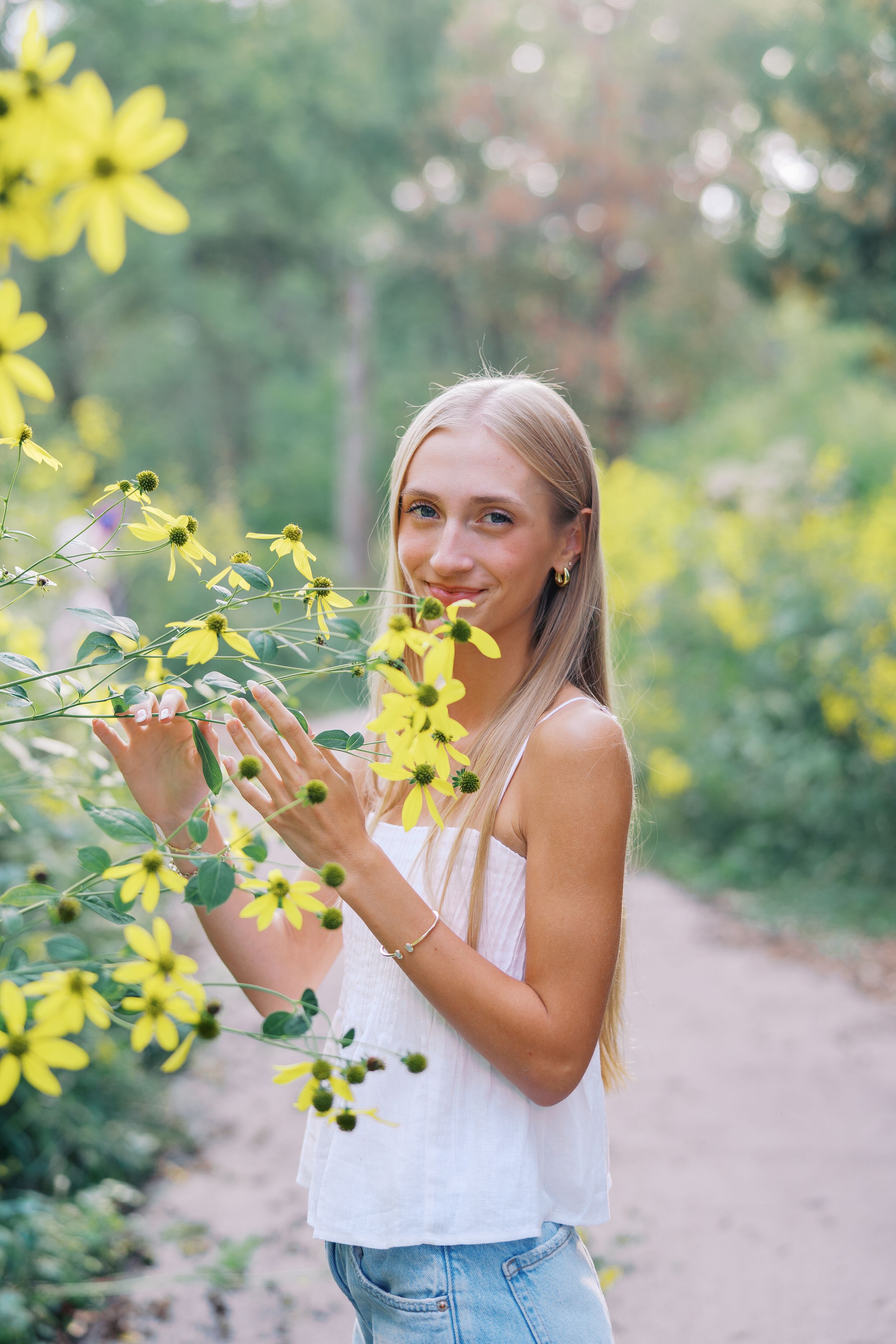 Someone smells bright yellow flowers along a garden path on a sunny day.