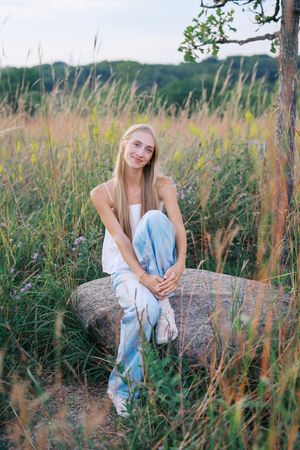 Rustic outdoor portrait session featuring poses on a large rock among wild grasses.