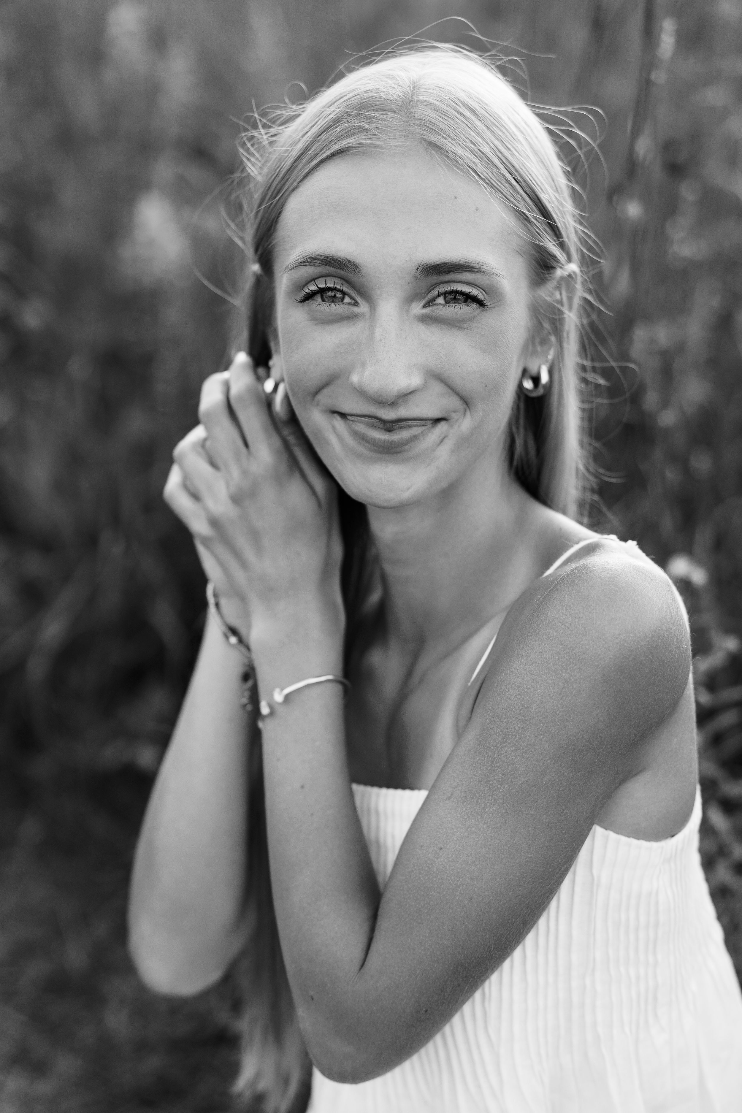 Black and white portrait of woman in white top smiling with hands near face.