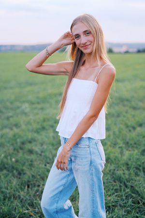 Woman in white top and light jeans poses playfully in grassy field.
