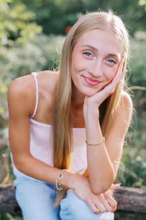 A person rests their chin on their hand while sitting outdoors in summer.