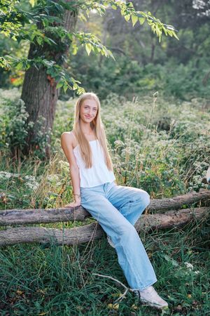 A person in casual attire sits on a fallen log in a lush green forest setting.