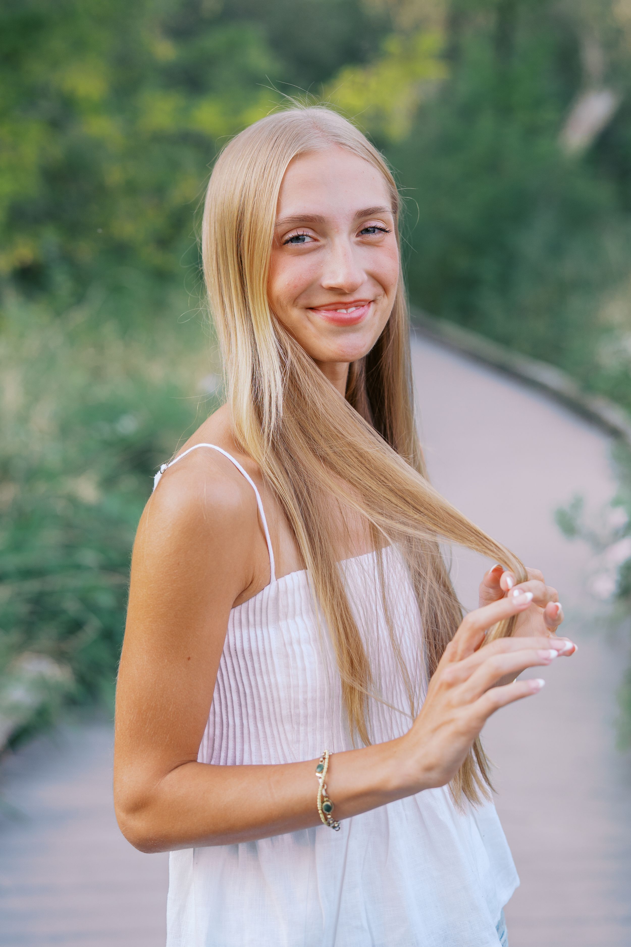A person in a white tank top smiles while enjoying a summer day outdoors.