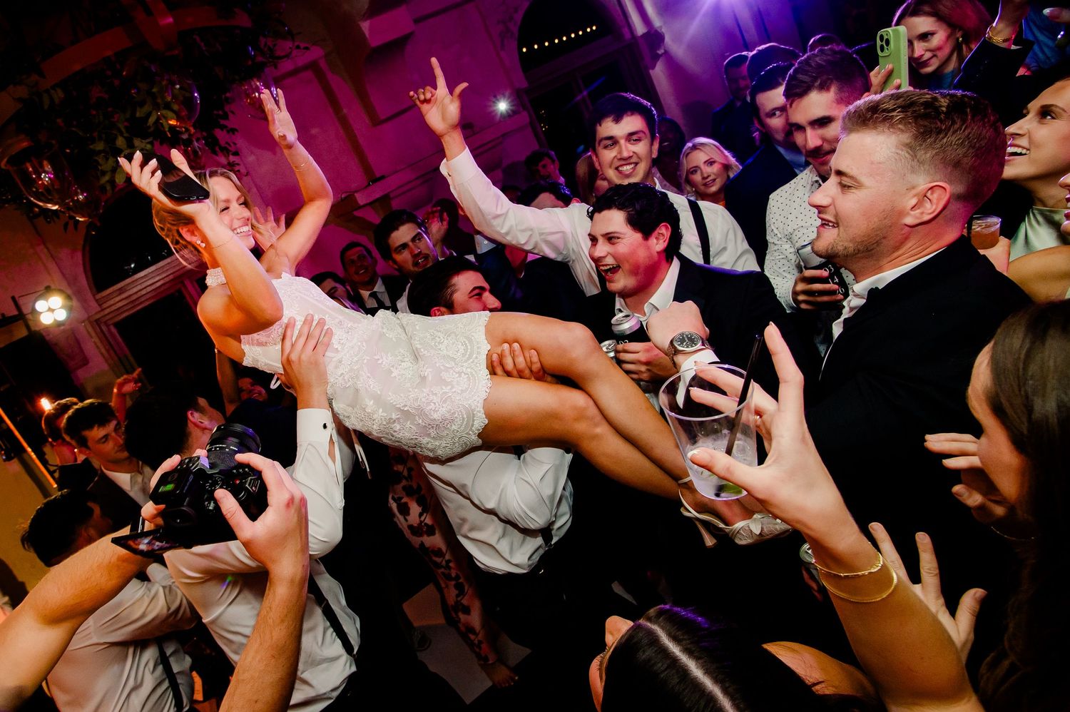 Energetic wedding reception crowd lifts and celebrates on a purple-lit dance floor during a lively party moment at Villa Antonia
