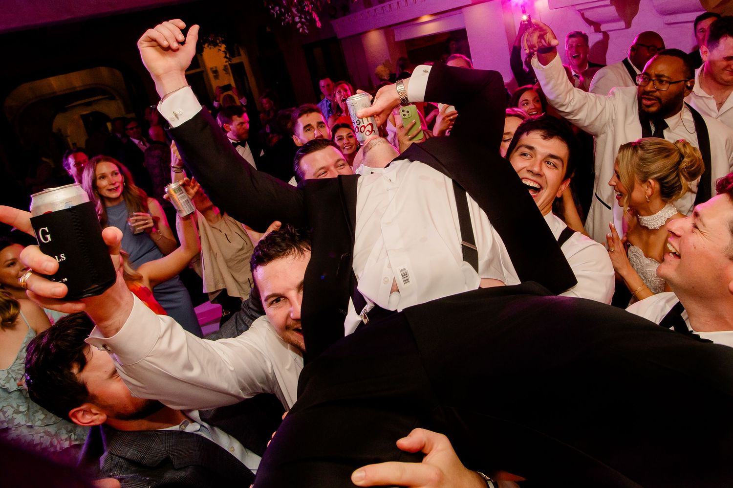 Energetic wedding reception dance party with guests celebrating on a crowded dance floor under pink lighting at Villa Antonia