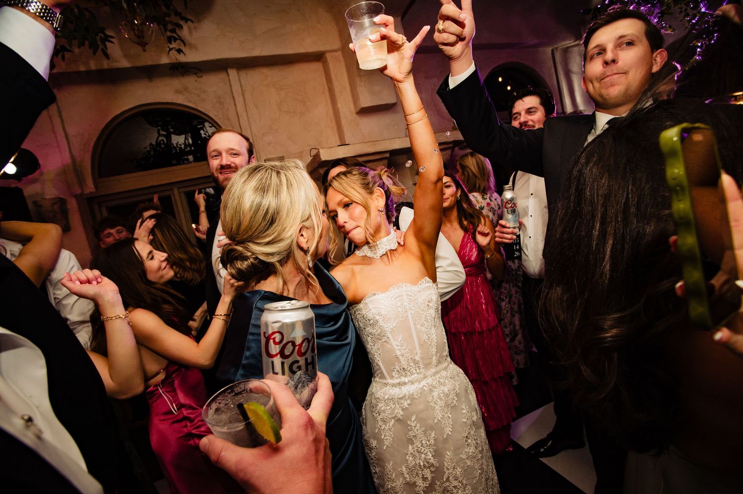 Wedding guests dancing and celebrating on a dimly lit dance floor during an evening reception party.