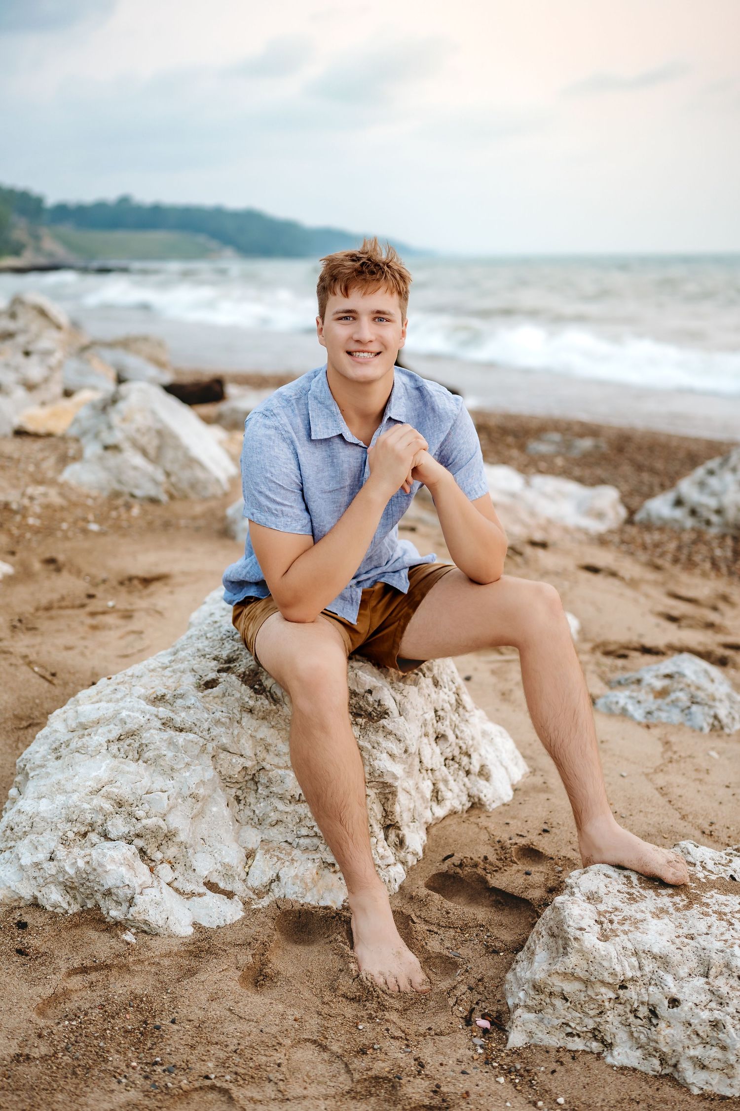 A casual beach portrait session on rocky coastal terrain with waves and mountains visible in the background.
