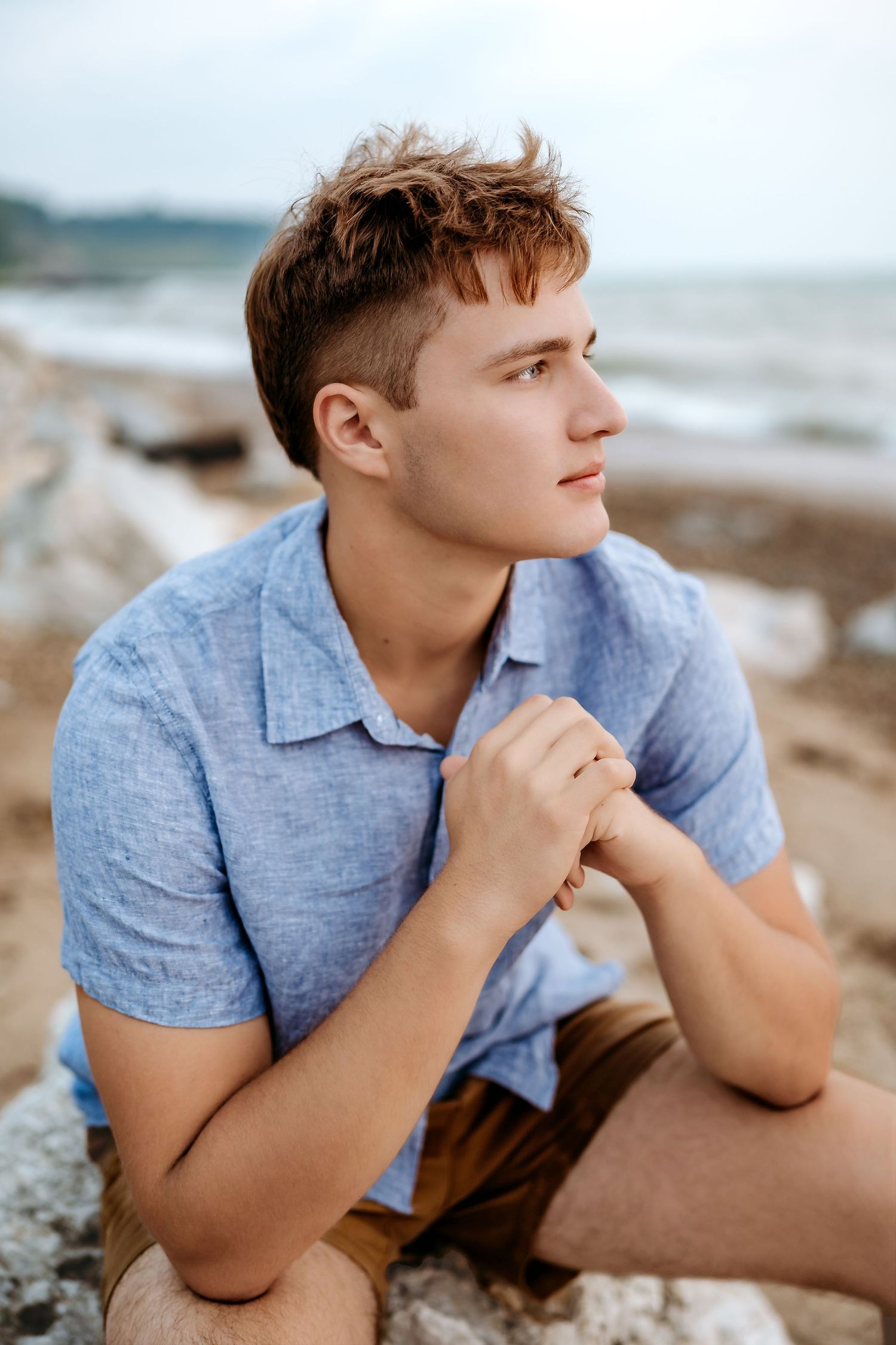 A person in a blue shirt lies thoughtfully on a beach with ocean waves in the background.