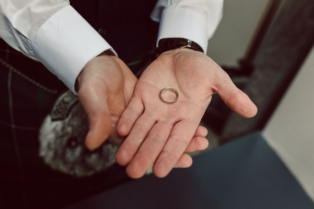 Two hands exchanging a gold wedding ring in a close-up shot during a ceremony.