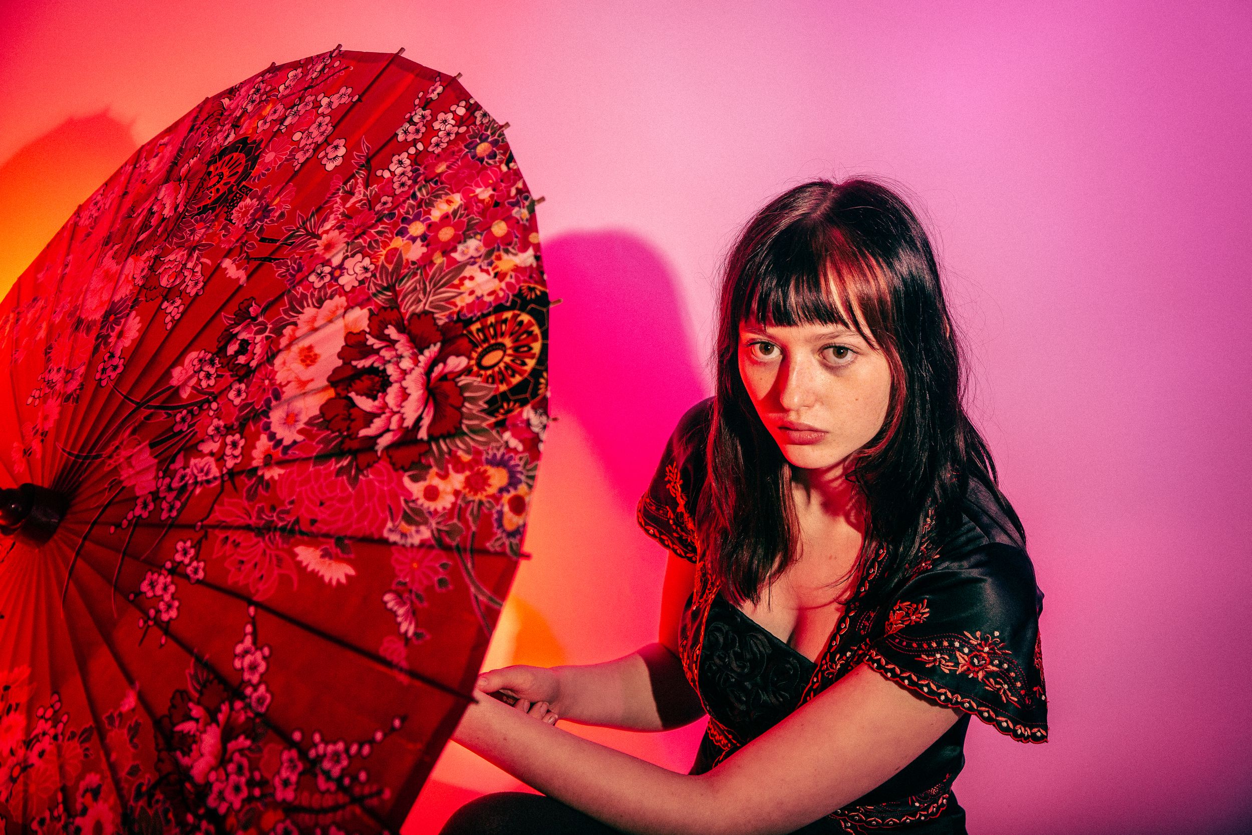 A series of artistic portraits with a red paper parasol against a vibrant pink and orange gradient background.
