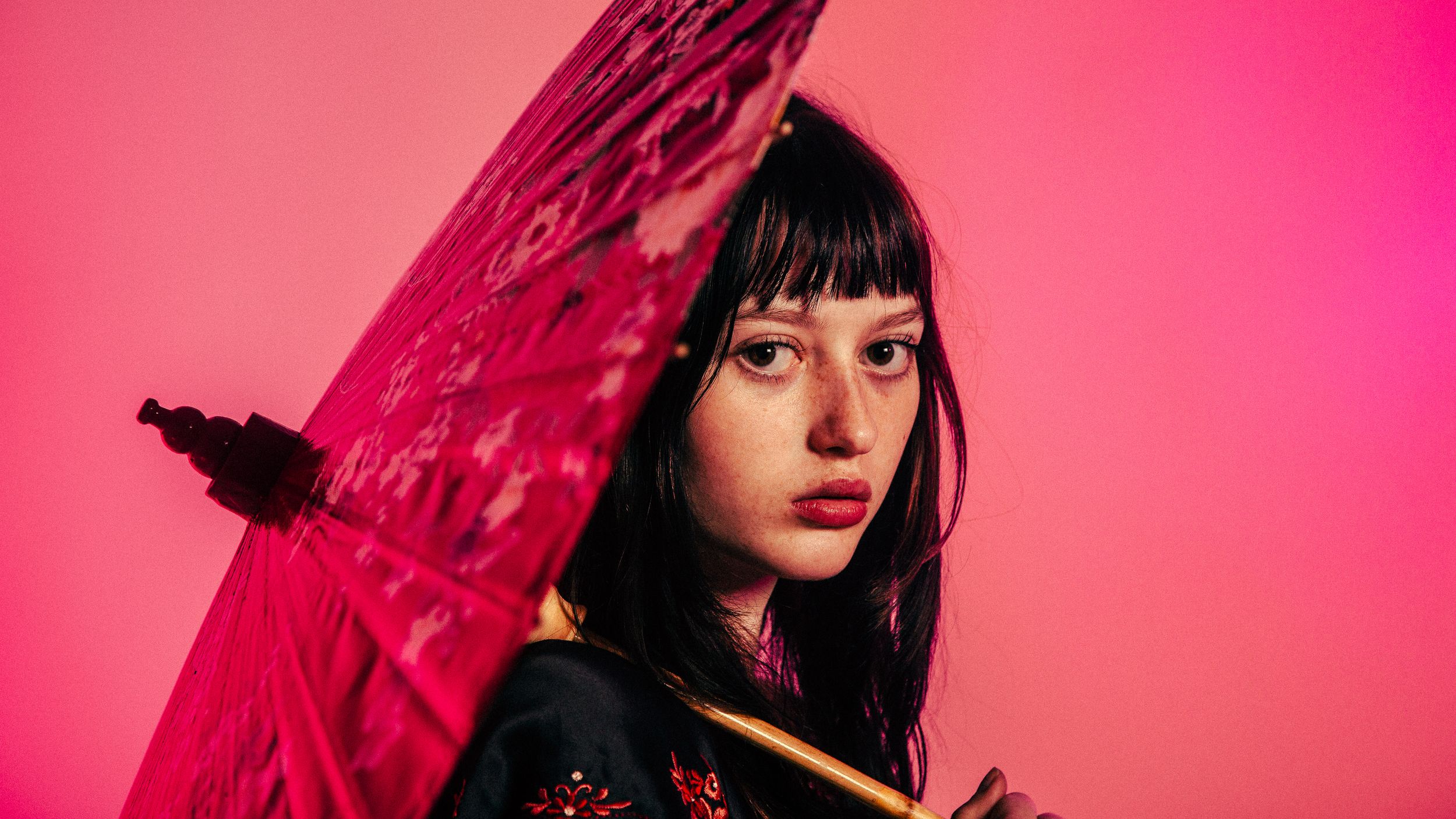 A woman in red lighting holds a red lace parasol while looking to the side in a series of artistic portraits.