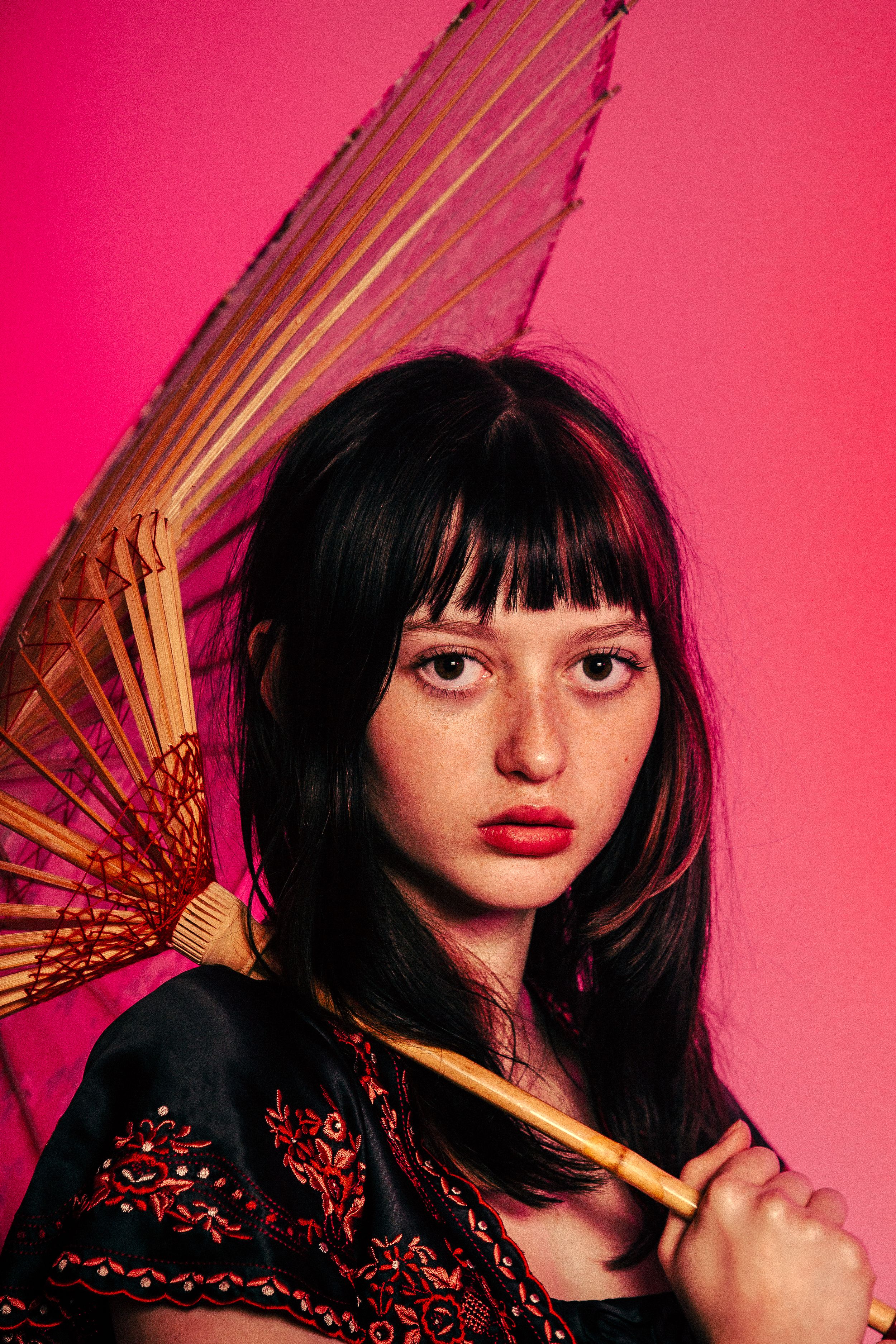 Artistic portrait series against pink backdrop featuring dark hair, red lipstick, and black lace outfit with dramatic lighting.