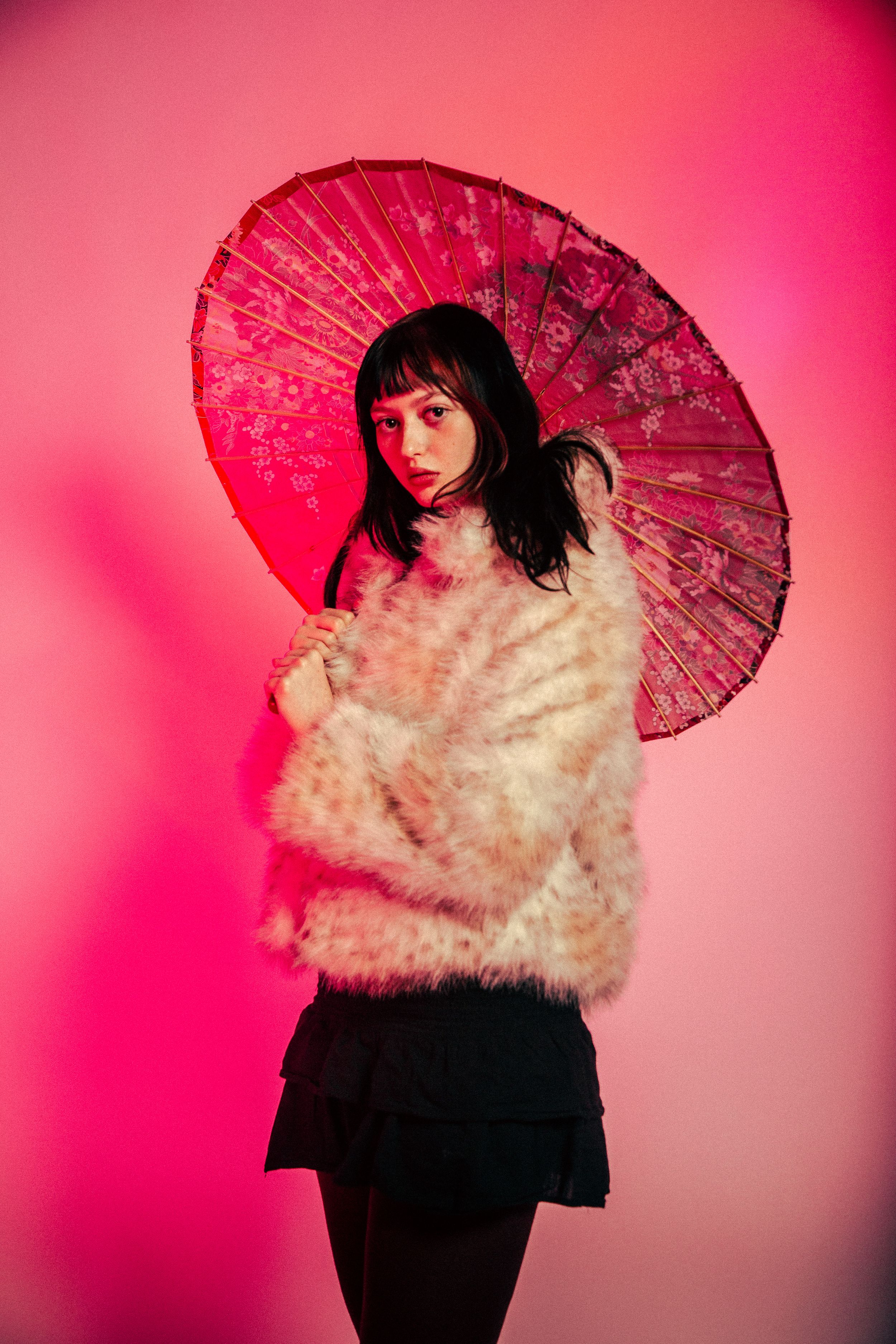 Fashion portrait with traditional red paper parasol against vibrant pink backdrop in artistic lighting.