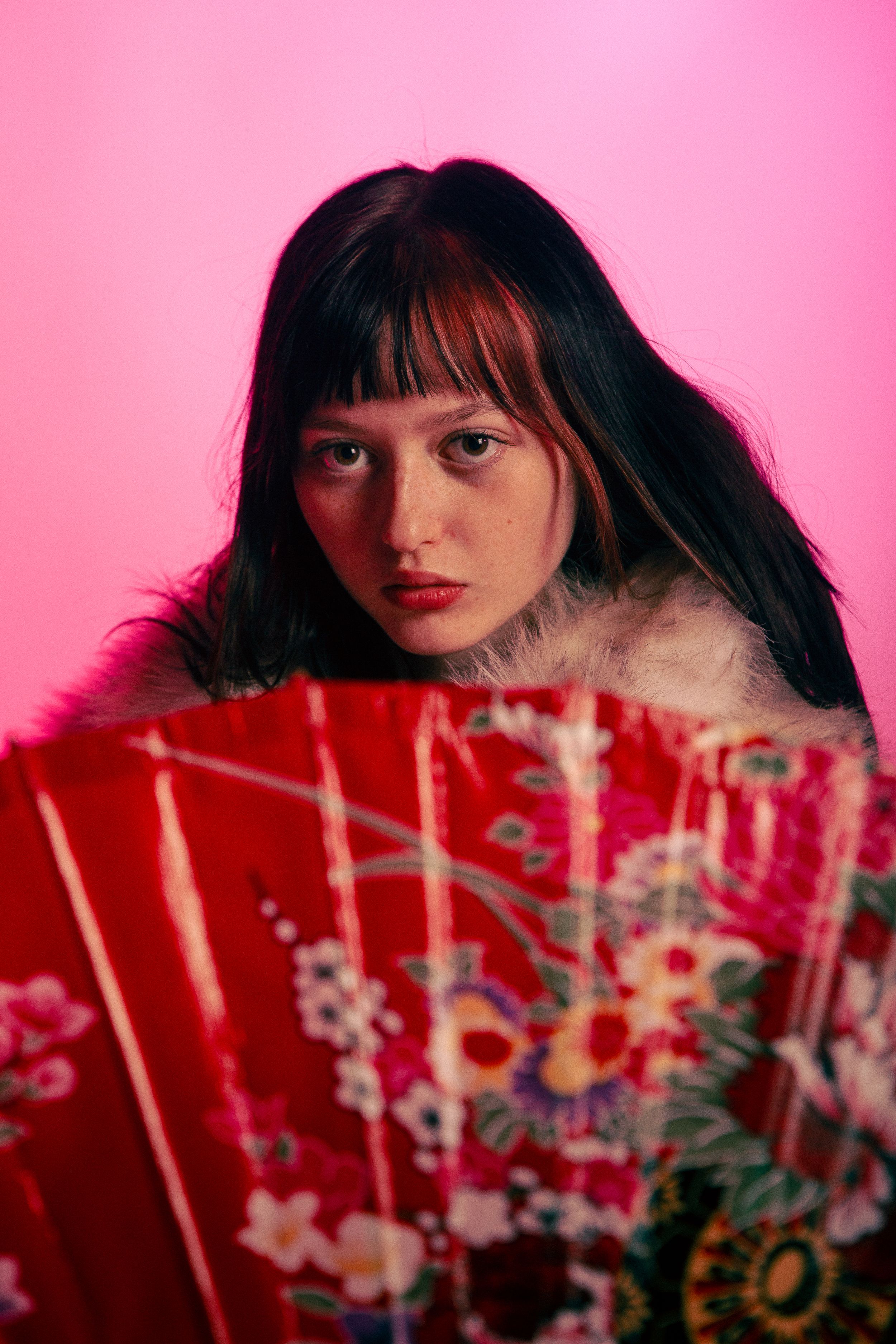 A vibrant pink and red portrait series with a decorative floral fan creating an artistic composition.