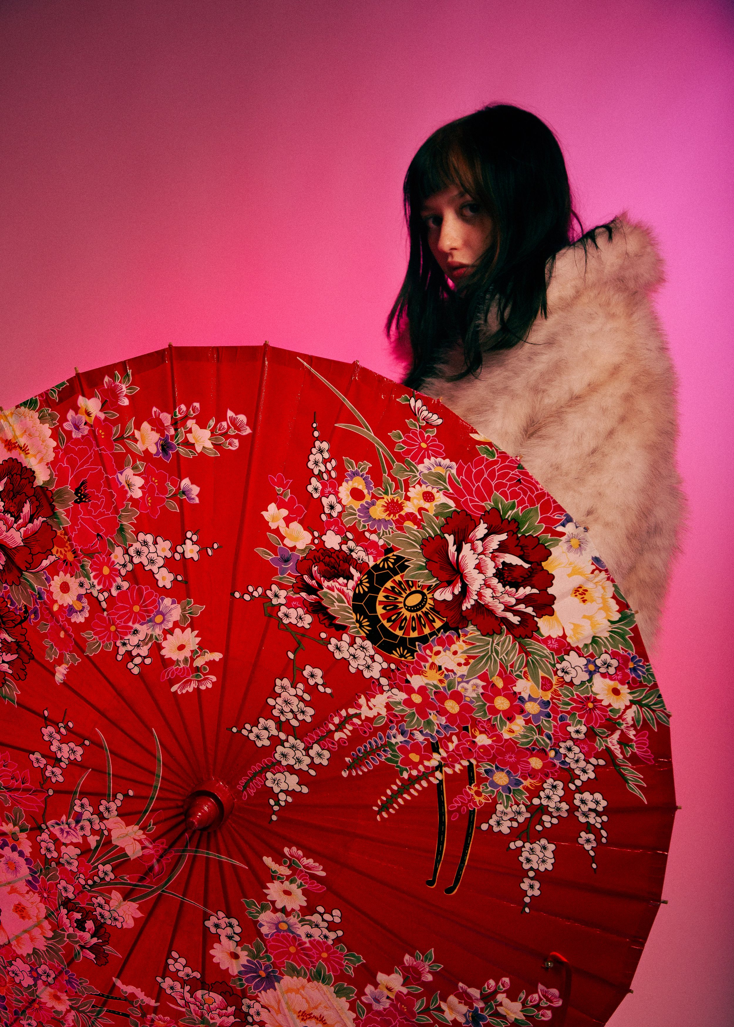 A red decorative Asian folding fan with delicate floral embroidery and blossoms against a pink background.