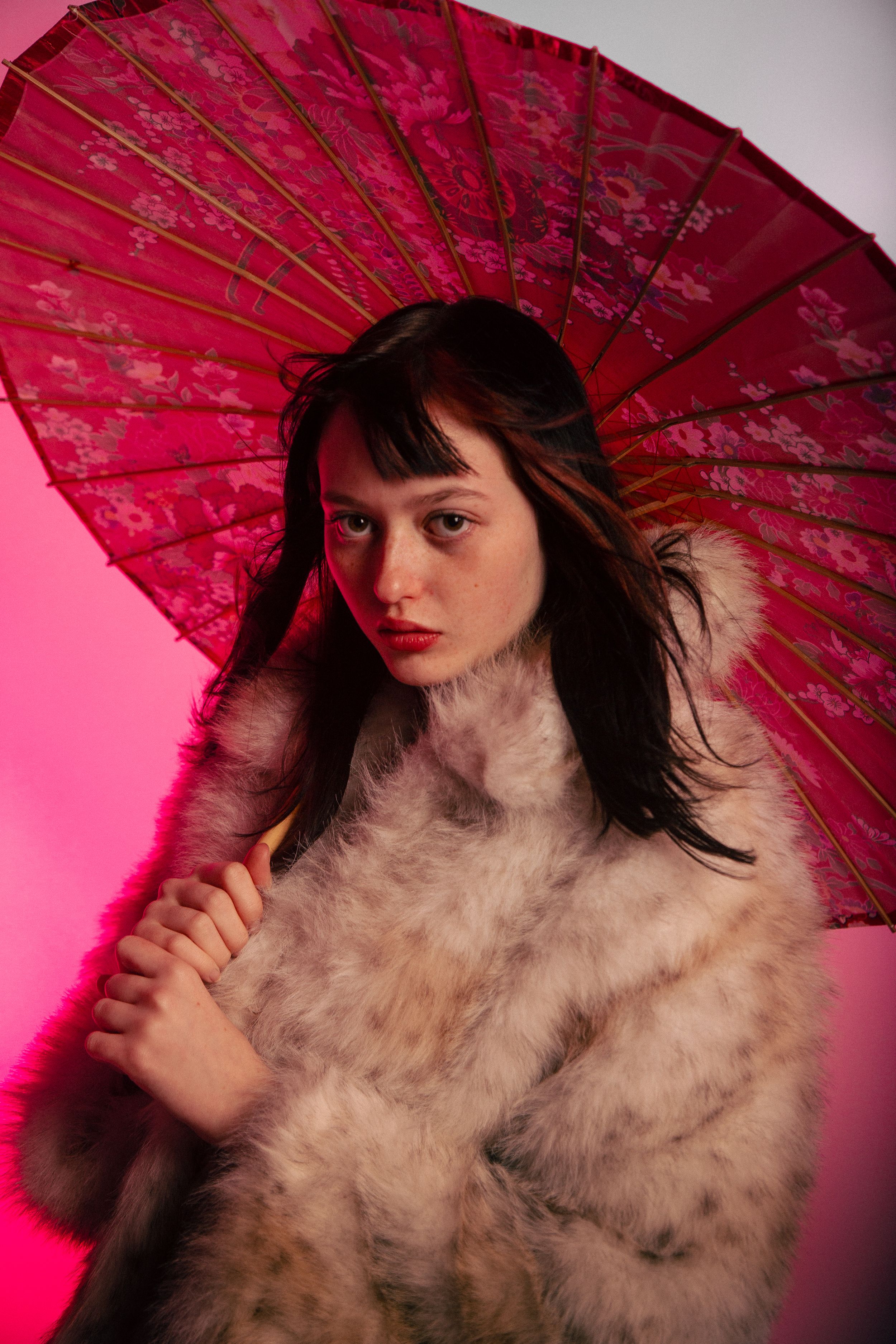 Dramatic fashion photo series with traditional Asian parasol and textured coat in vibrant pink lighting.