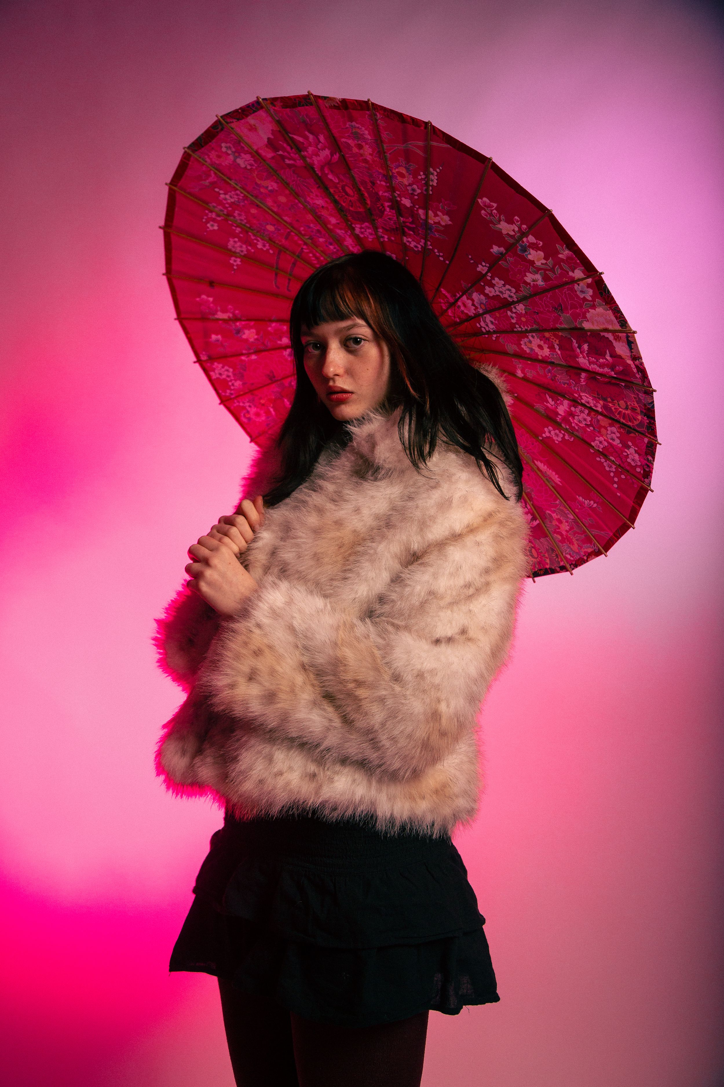 A series of artistic portraits featuring a red parasol and fur stole against a vibrant pink background.