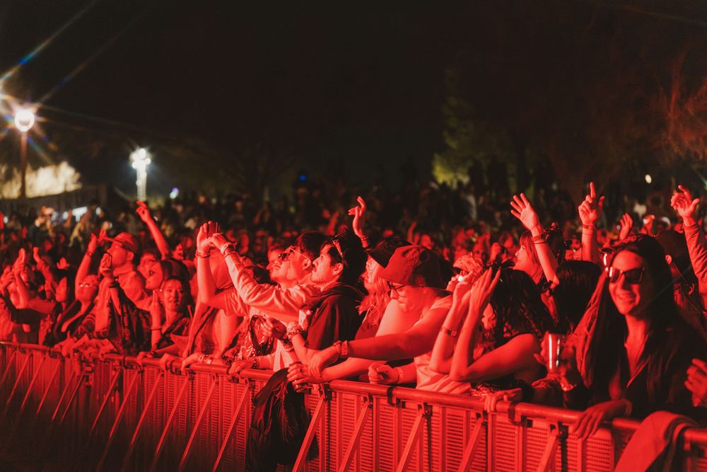 Concert crowd illuminated in red light raises their hands during a live performance at night.
