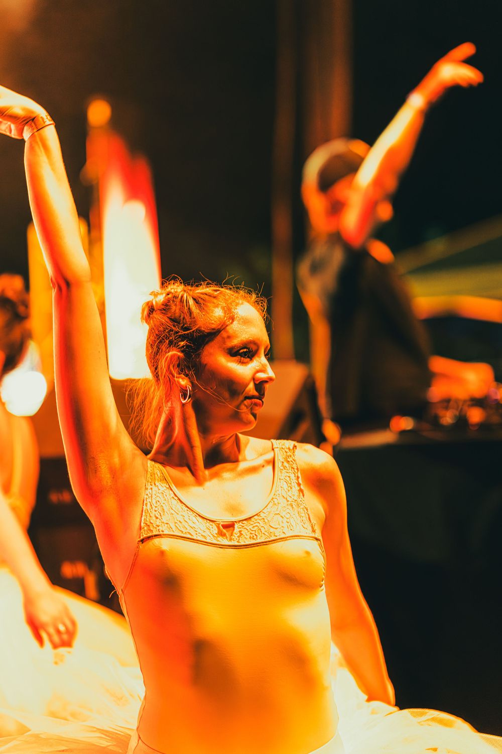 Dancers perform in warm orange lighting with raised arms during an energetic stage performance.