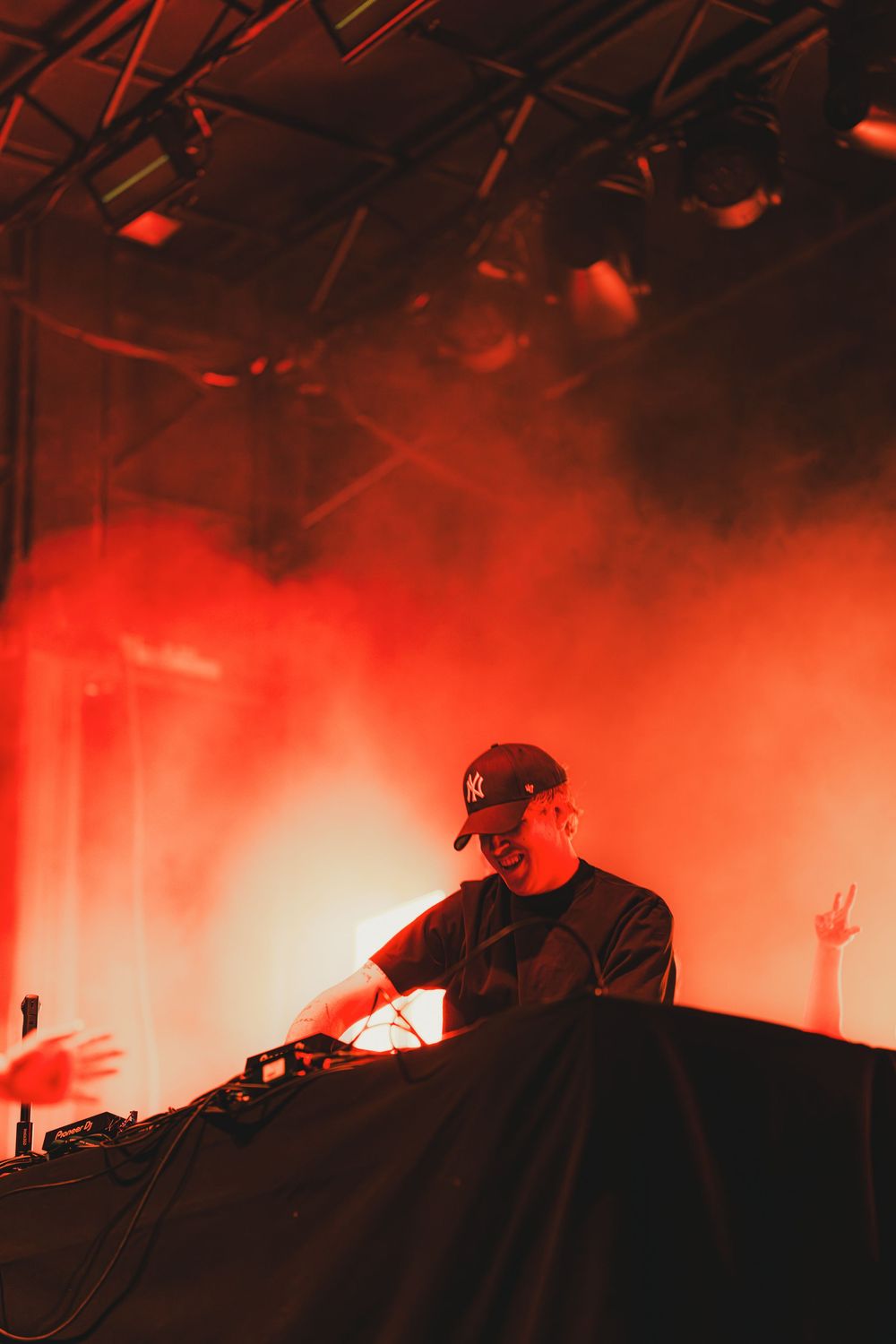 DJ performs at an electronic music event with dramatic red lighting and fog effects on stage.