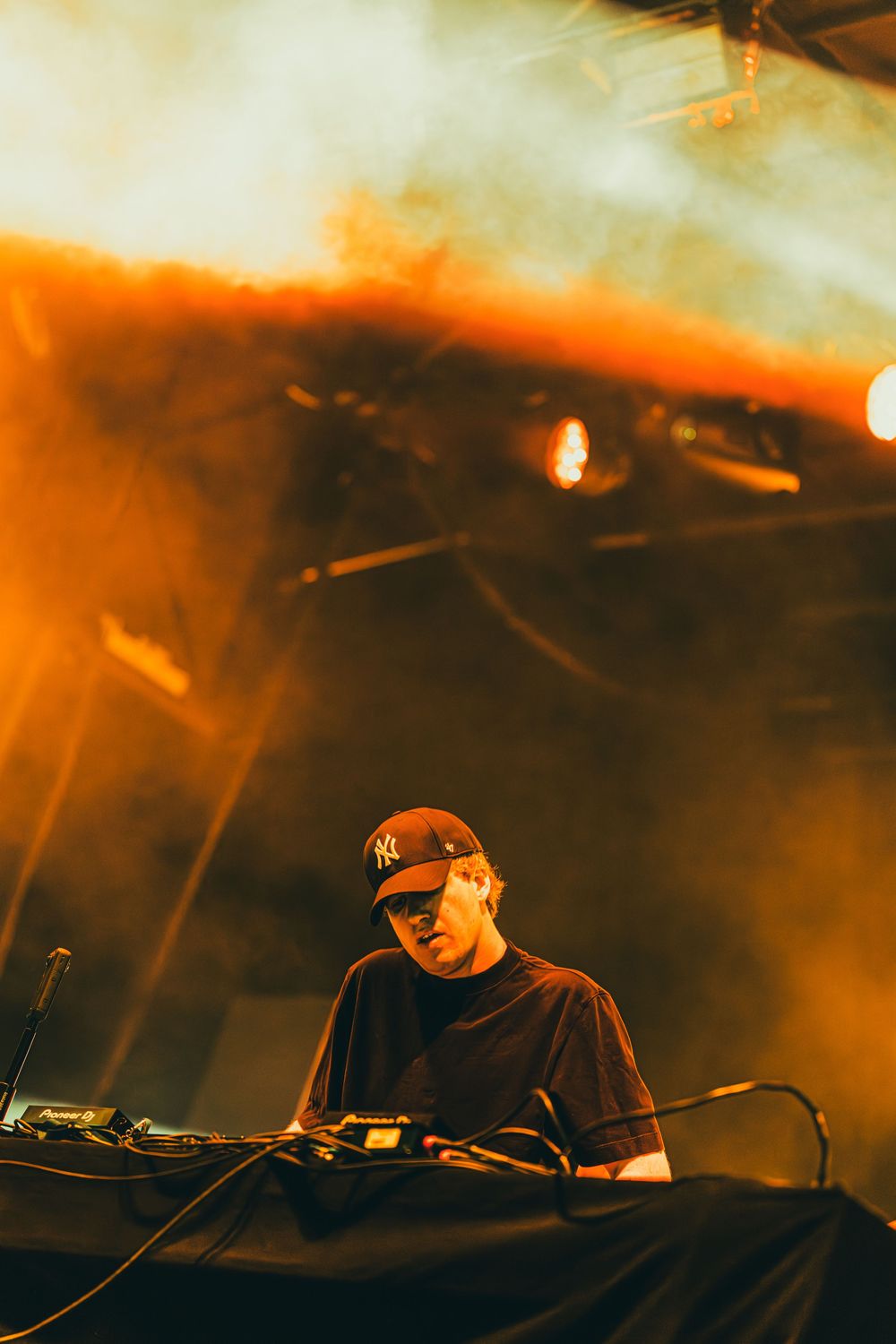 DJ performs at a dimly lit venue with orange lighting and electronic equipment creating an atmospheric ambiance.